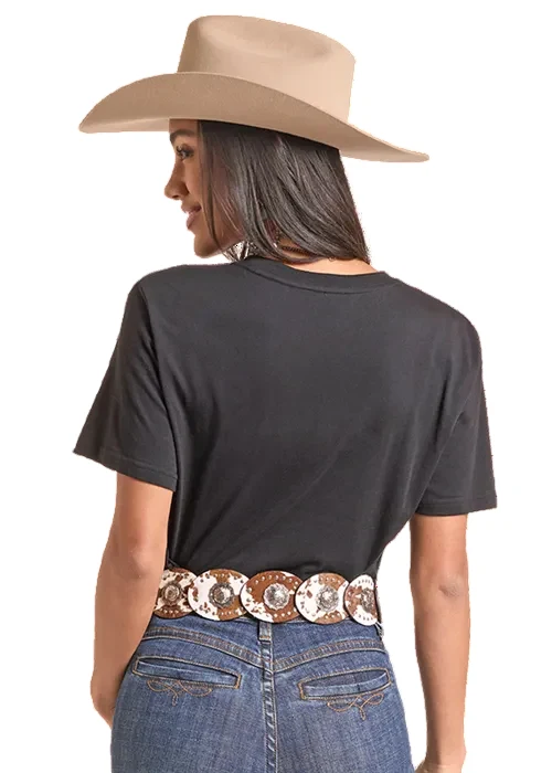 A woman shown from the back wearing a beige wide-brim cowboy hat, a black short-sleeve t-shirt, a western-style belt with large silver conchos, and blue jeans, against a plain white background.