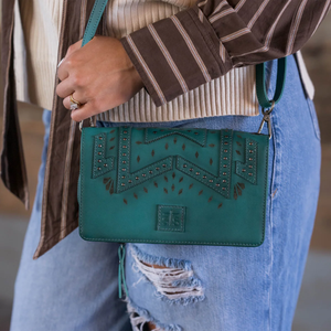 Person holding a green handbag with decorative elements, wearing a striped sweater and ripped jeans.