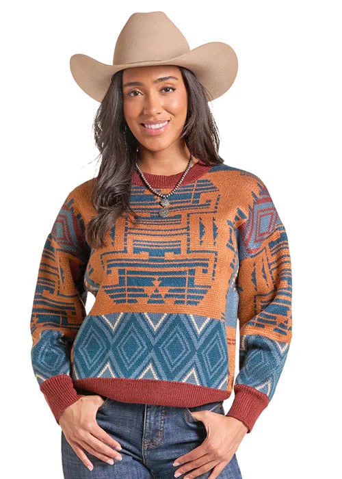 A woman wearing a southwestern-style knit sweater with geometric patterns in rust orange, teal blue, and burgundy, paired with a tan cowboy hat and blue jeans, against a plain white background.