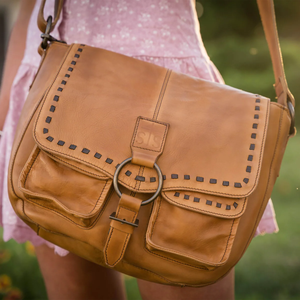 Brown leather bag with decorative studs held by a person wearing a pink dress.