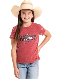 Young girl wearing a red t-shirt with a cow print and a straw hat.