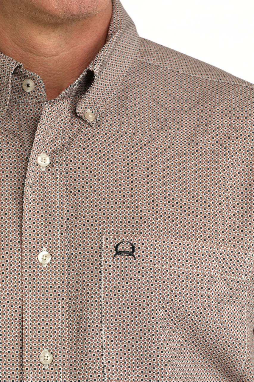 Close-up of a man wearing a brown and beige micro-patterned button-down shirt with a chest pocket and a small black embroidered logo.