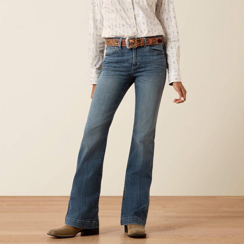 Person wearing blue jeans and a patterned shirt on a plain background