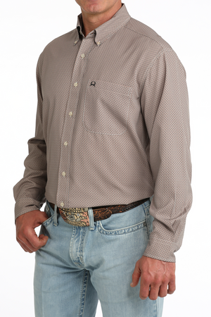 A man wearing a light brown long-sleeve western-style button-down shirt with a subtle micro-pattern, paired with light blue jeans and a brown leather belt with a silver buckle.