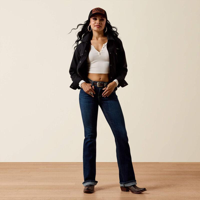 Woman wearing a black jacket, white top, blue jeans, and brown boots against a beige background
