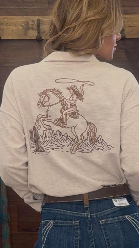 Person wearing a beige shirt with a graphic of a cowgirl on a horse and cactus.