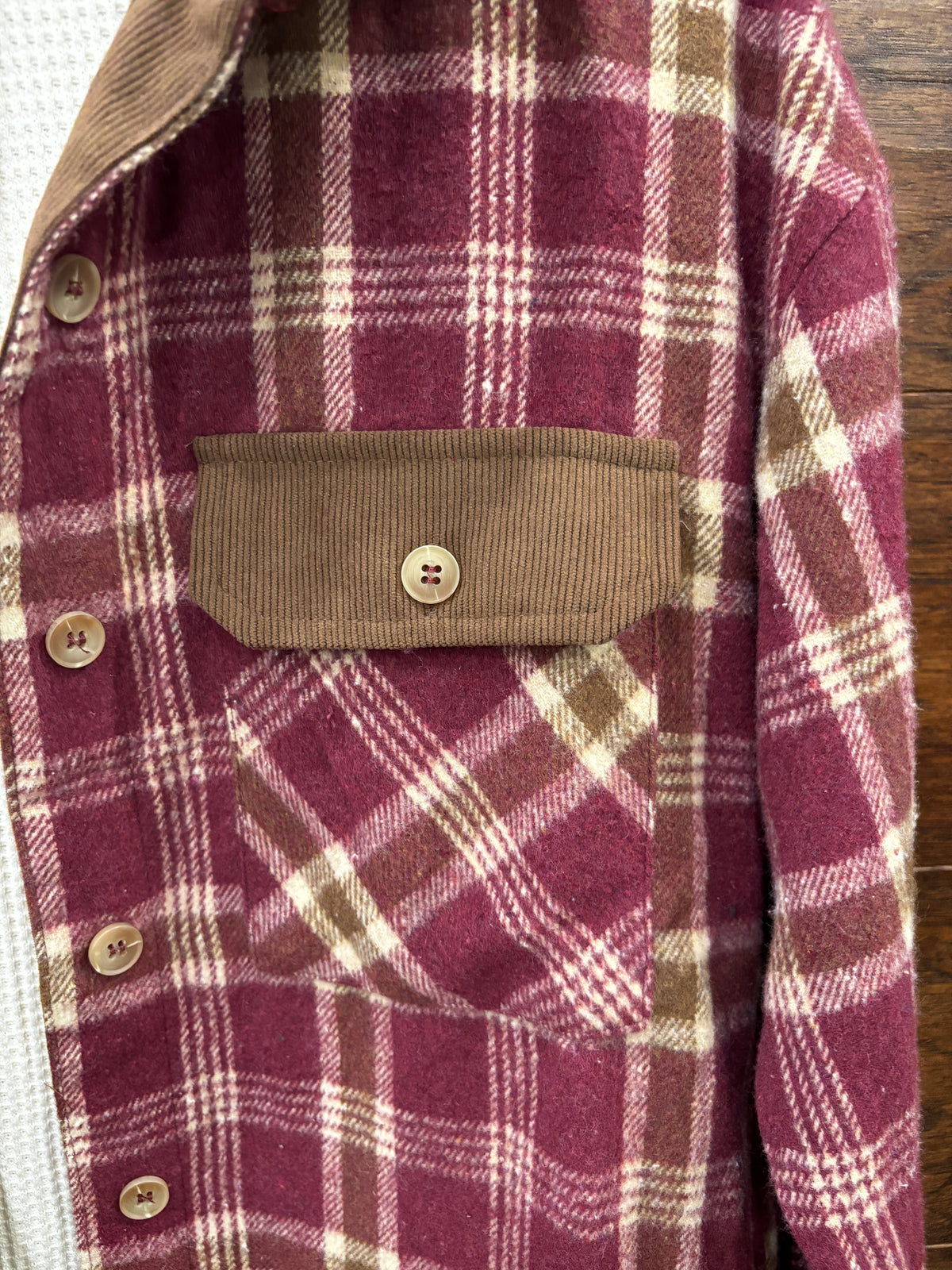 A burgundy and beige plaid flannel shirt with a brown corduroy collar and chest pockets