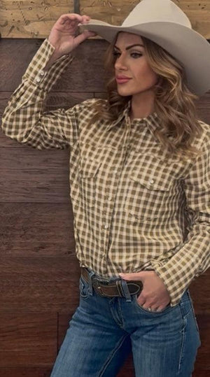 Woman wearing a plaid shirt, jeans, and a wide-brimmed hat against a wooden background