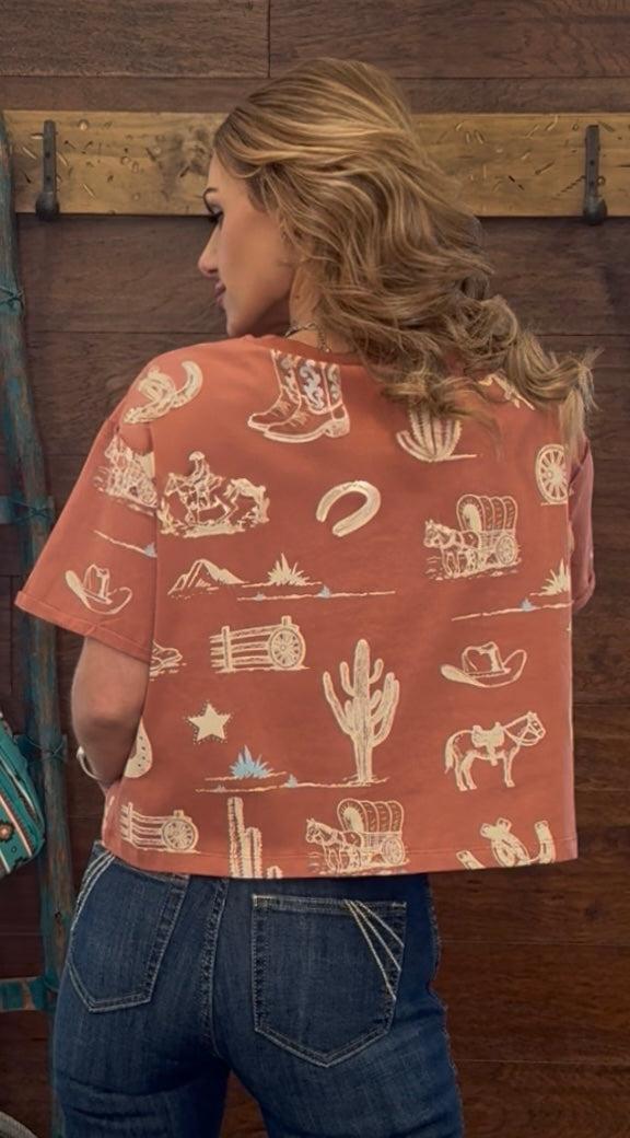 Person wearing a red shirt with western-themed patterns against a wooden background