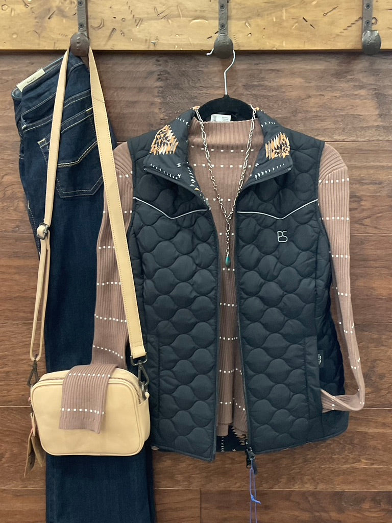 A black quilted sleeveless vest with geometric patterned shoulder panels and white piping, layered over a brown ribbed knit sweater. 