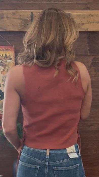 Person wearing a red tank top and blue jeans standing in front of a wooden wall with posters.