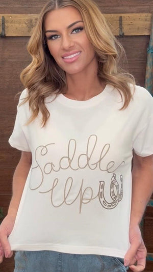 Woman wearing a white t-shirt with 'Saddle Up' text and horseshoe design.