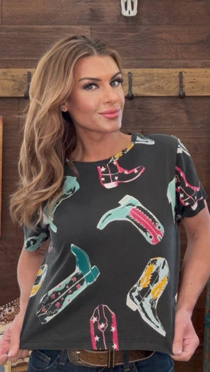 Woman wearing a black t-shirt with colorful shoe designs against a wooden wall.