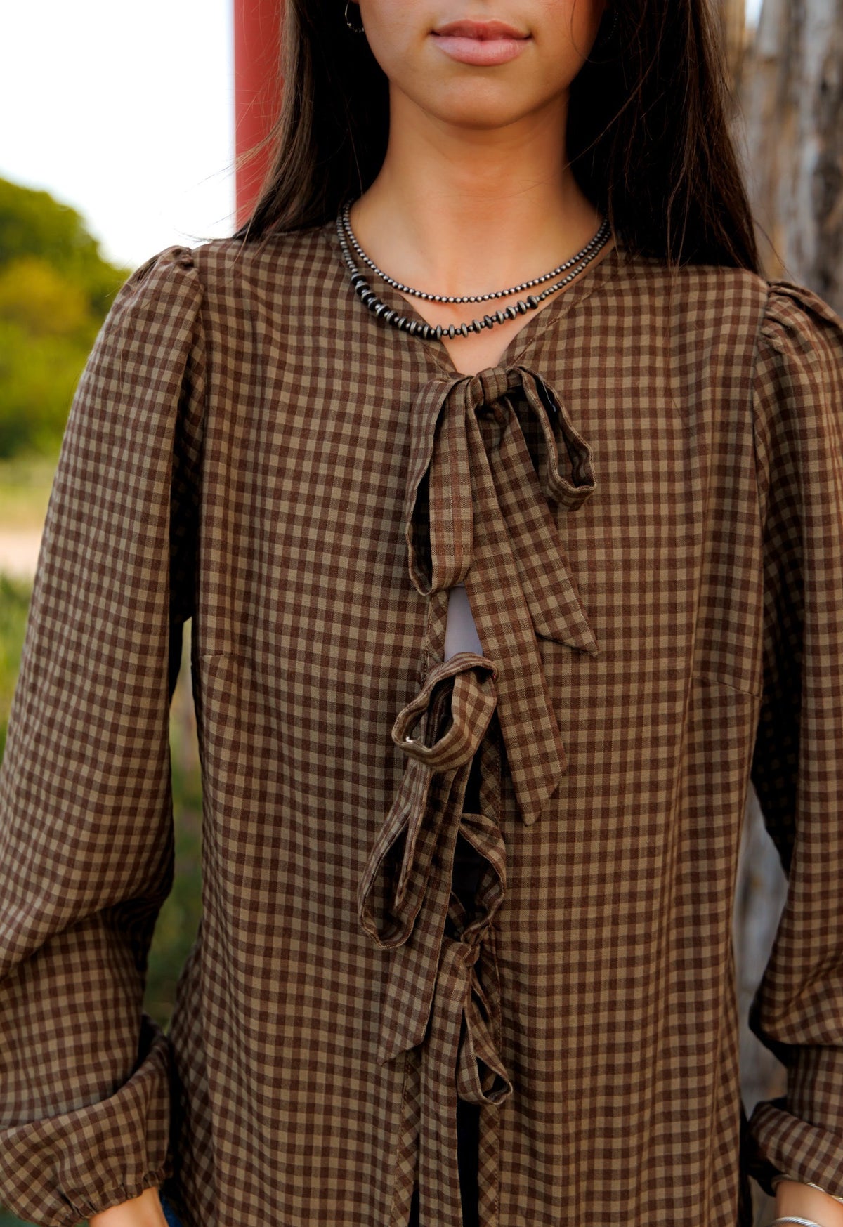 This charming blouse features a timeless brown checkered pattern and a stylish front tie detail, making it a versatile and fashionable addition to any wardrobe.