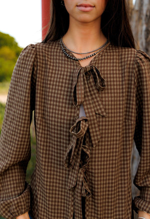 This charming blouse features a timeless brown checkered pattern and a stylish front tie detail, making it a versatile and fashionable addition to any wardrobe.