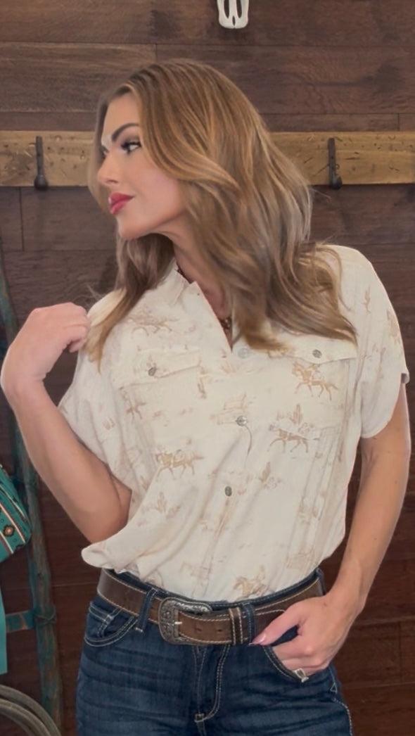 Woman wearing a white blouse with patterns and blue jeans against a wooden background
