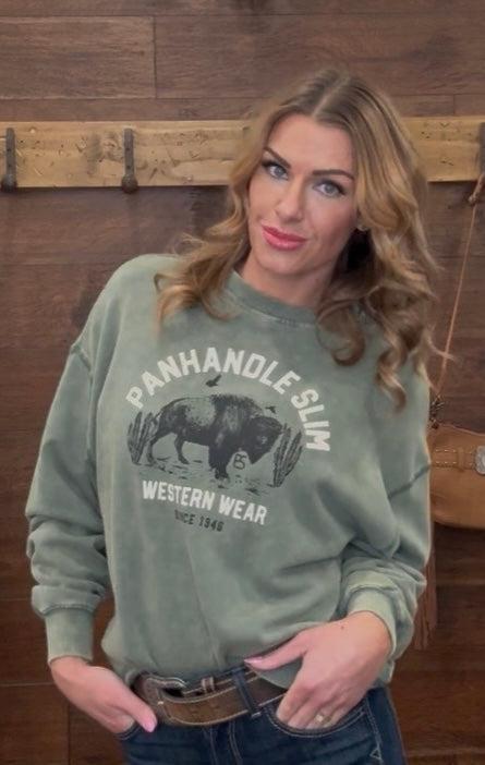 Woman wearing a green sweatshirt with 'Panhandle Slim Western Wear' logo against a wooden wall.