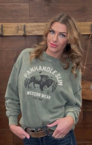 Woman wearing a green sweatshirt with 'Panhandle Slim Western Wear' logo against a wooden wall.