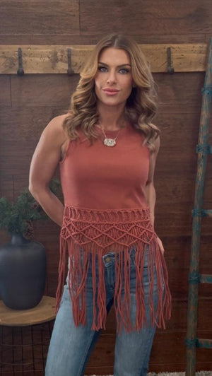 Woman wearing a rust-colored fringe top against a wooden wall.