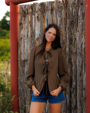 This charming blouse features a timeless brown checkered pattern and a stylish front tie detail, making it a versatile and fashionable addition to any wardrobe.