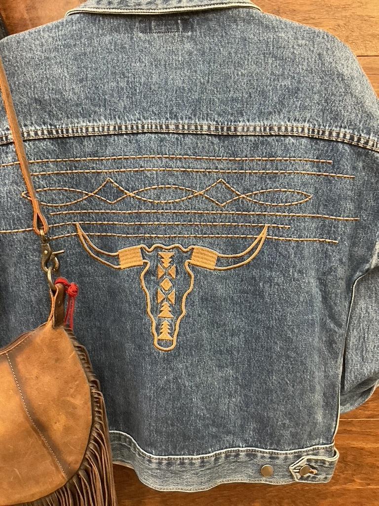 A blue denim jacket with a large embroidered steer skull design on the back. 