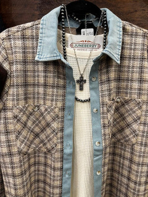A plaid button-up shirt with a light blue denim collar and cuffs layered over a white knit shirt, hanging on a wooden wall rack next to dark blue jeans and a brown leather pouch.