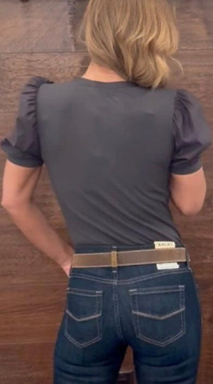 Woman wearing a gray short-sleeve shirt with a wooden wall and decorative items in the background