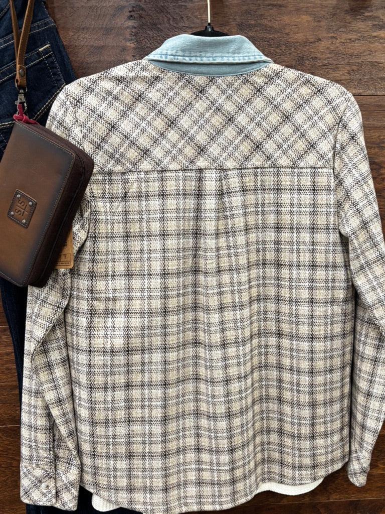 A long-sleeve plaid overshirt with a light blue collar, shown hanging on a wooden surface next to a brown leather crossbody bag and blue jeans.