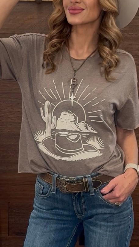 Person wearing a gray t-shirt with a graphic design, standing against a wooden background