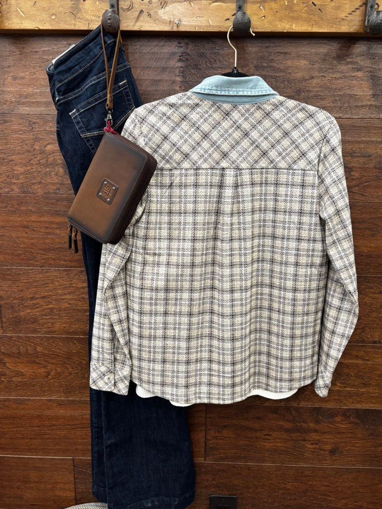 A long-sleeve plaid button-up shirt in beige, brown, and gray hangs on a wooden wall alongside dark blue jeans and a brown leather pouch.
