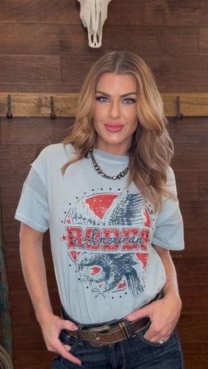 Woman wearing a graphic t-shirt with an eagle design in a rustic setting.