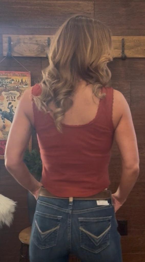 Person wearing a red tank top and blue jeans standing in a room with wooden walls and a poster.