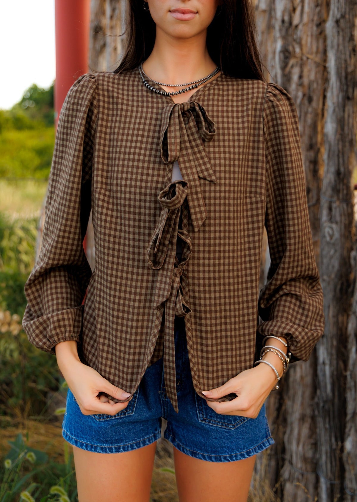 This charming blouse features a timeless brown checkered pattern and a stylish front tie detail, making it a versatile and fashionable addition to any wardrobe.
