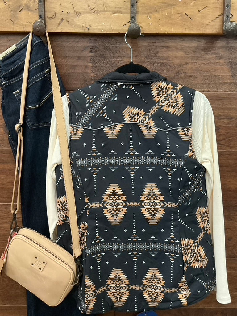 A sleeveless patterned vest with a black base and beige geometric Southwestern-style motifs, layered over a cream long-sleeve shirt 