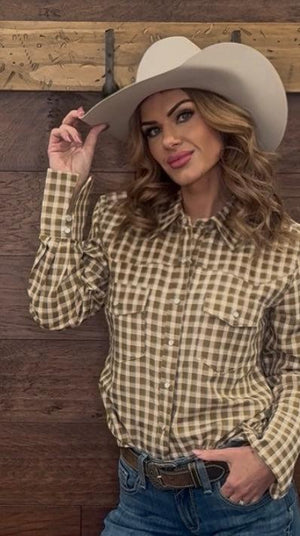 Woman wearing a checkered shirt and cowboy hat against a wooden wall.