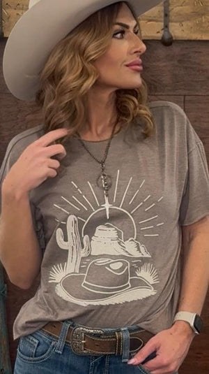 Woman wearing a gray t-shirt with a graphic design, sitting against a wooden wall.