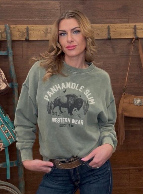 Woman wearing a green sweatshirt with 'Panhandle Slim Western Wear' logo in a rustic setting.
