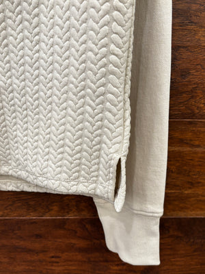 A cream-colored quarter-zip pullover sweater with a textured chevron pattern on the lower half