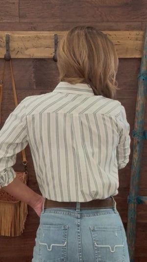 Person wearing a striped shirt and jeans standing in front of a wooden wall.