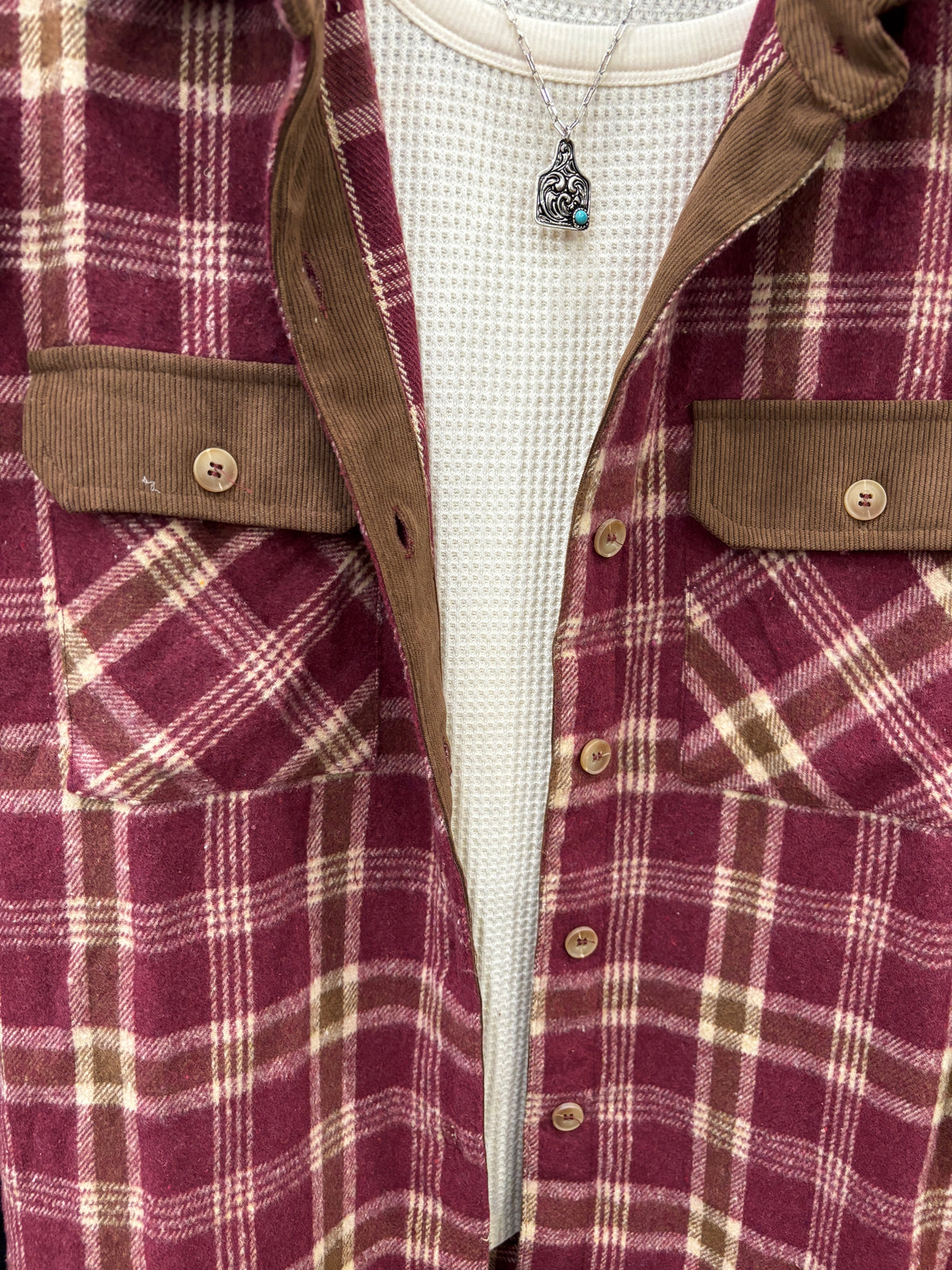 A burgundy and beige plaid flannel shirt with a brown corduroy collar and chest pockets