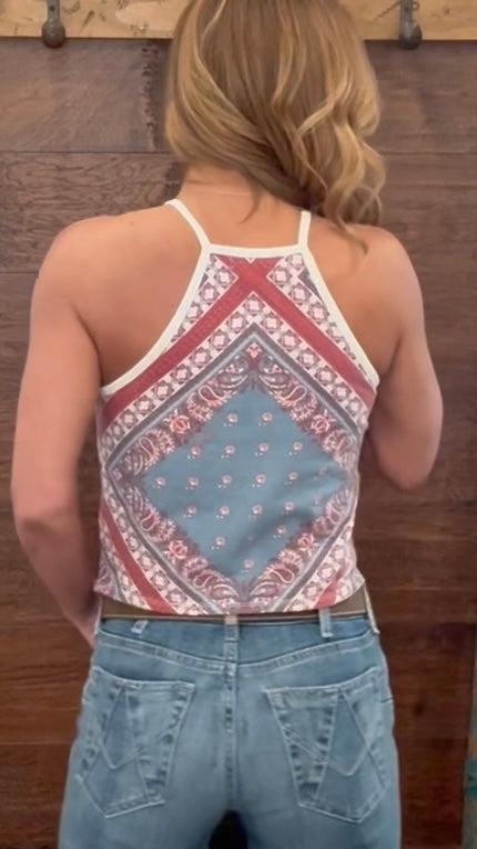 Person wearing a patterned tank top and jeans against a wooden background