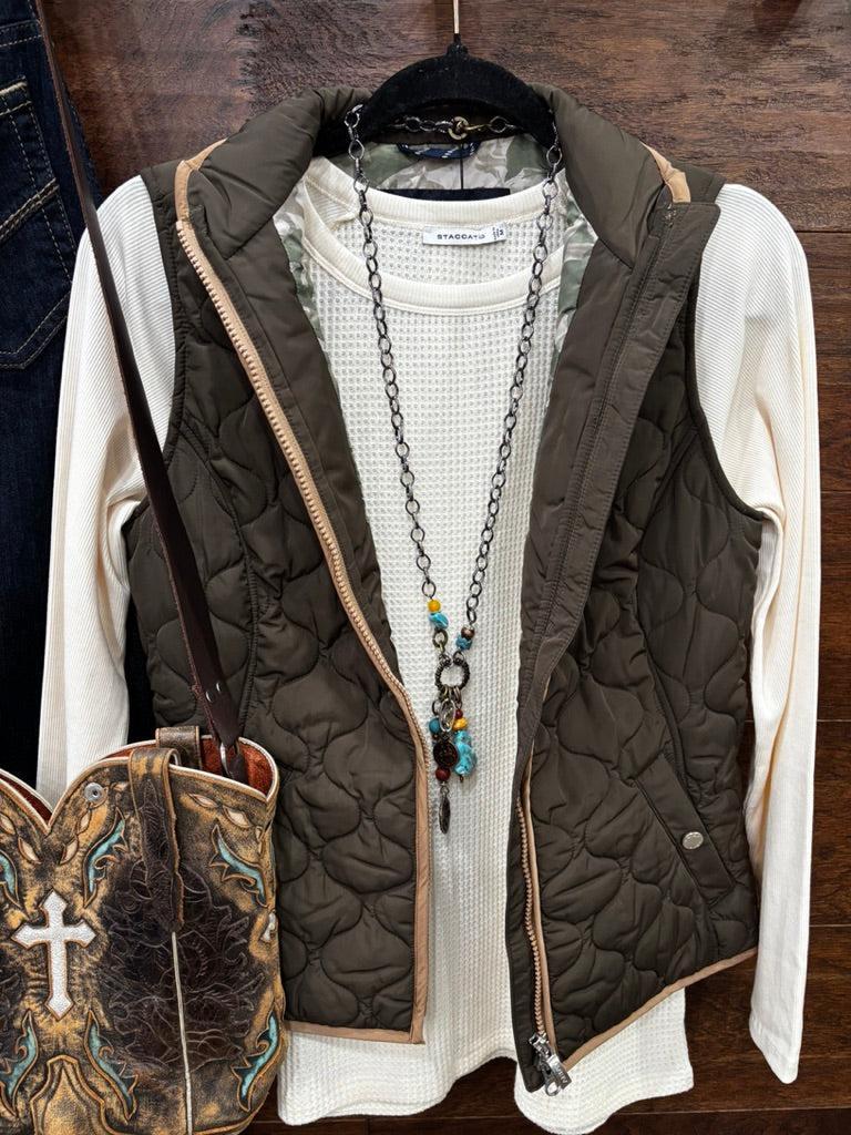 An earth tome quilted zip-up vest layered over a cream knit sweater