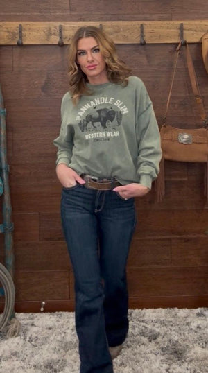 Woman wearing a green sweatshirt with a graphic design in front of a wooden wall.