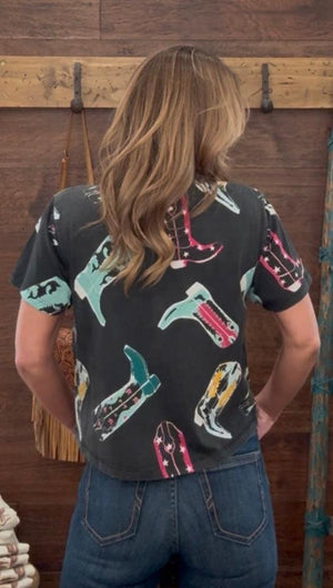 Person wearing a black shirt with colorful boot designs in front of a wooden wall.