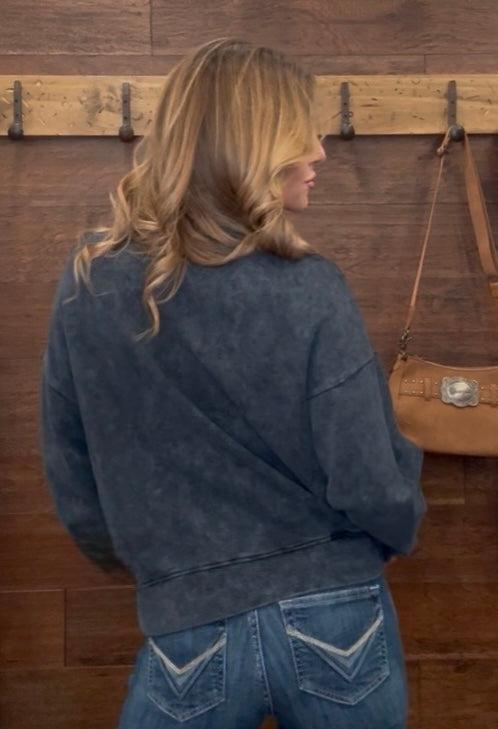 Woman wearing a dark gray sweatshirt with graphic design and text, standing against a wooden wall.