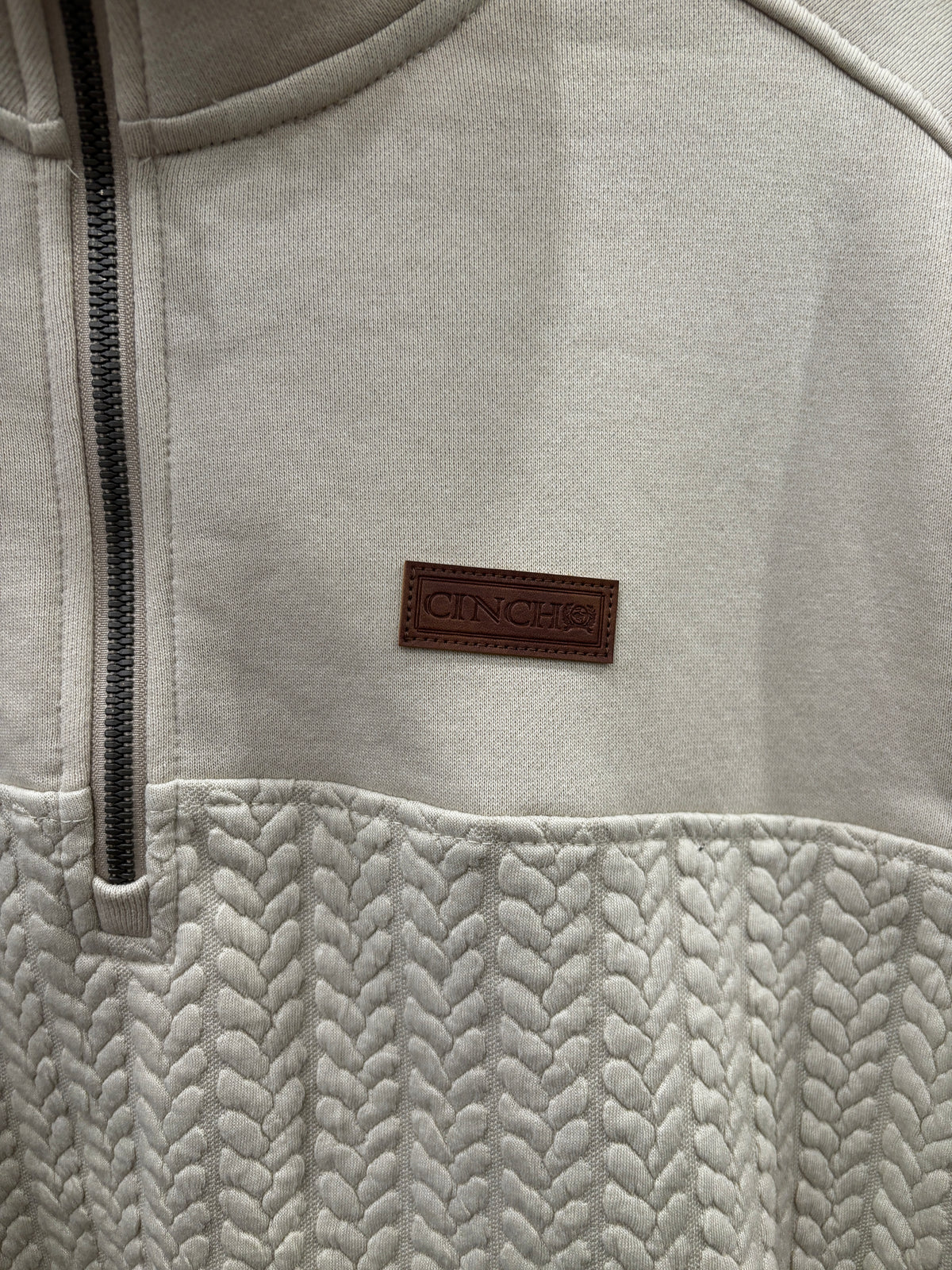 A cream-colored quarter-zip pullover sweater with a textured chevron pattern on the lower half