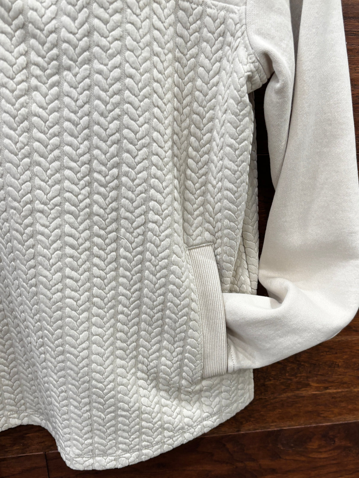 A cream-colored quarter-zip pullover sweater with a textured chevron pattern on the lower half