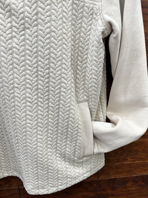 A cream-colored quarter-zip pullover sweater with a textured chevron pattern on the lower half