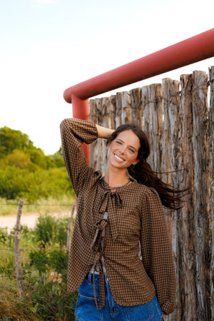 This charming blouse features a timeless brown checkered pattern and a stylish front tie detail, making it a versatile and fashionable addition to any wardrobe.