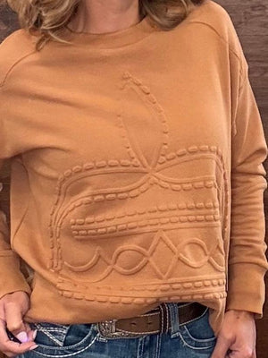 A person wearing a camel-colored long-sleeve knit sweater with a raised geometric pattern on the front, paired with blue jeans and a brown belt.